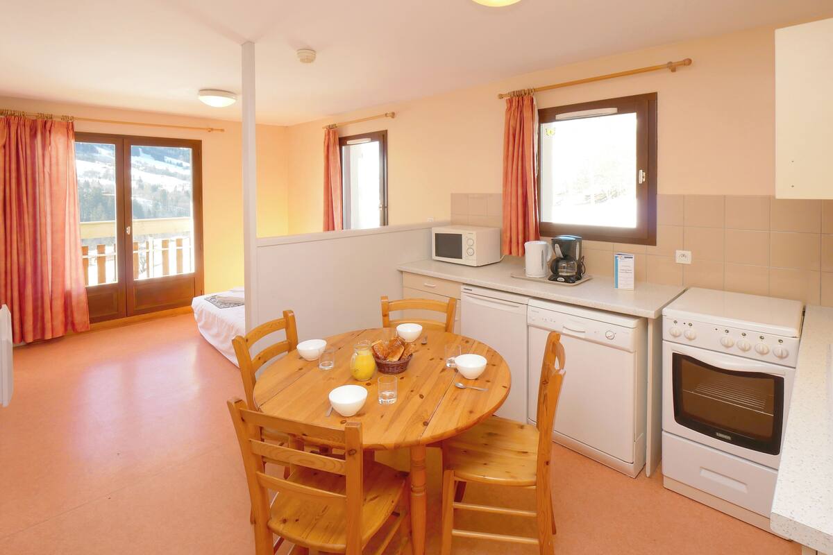 A compact kitchen with a dining table, chairs, a microwave, a coffee maker, and a stove.