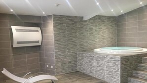 A modern bathroom with a stone wall, a bathtub, and two lounge chairs. - Les Essertets - Vacances ULVF (Praz-sur-Arly)