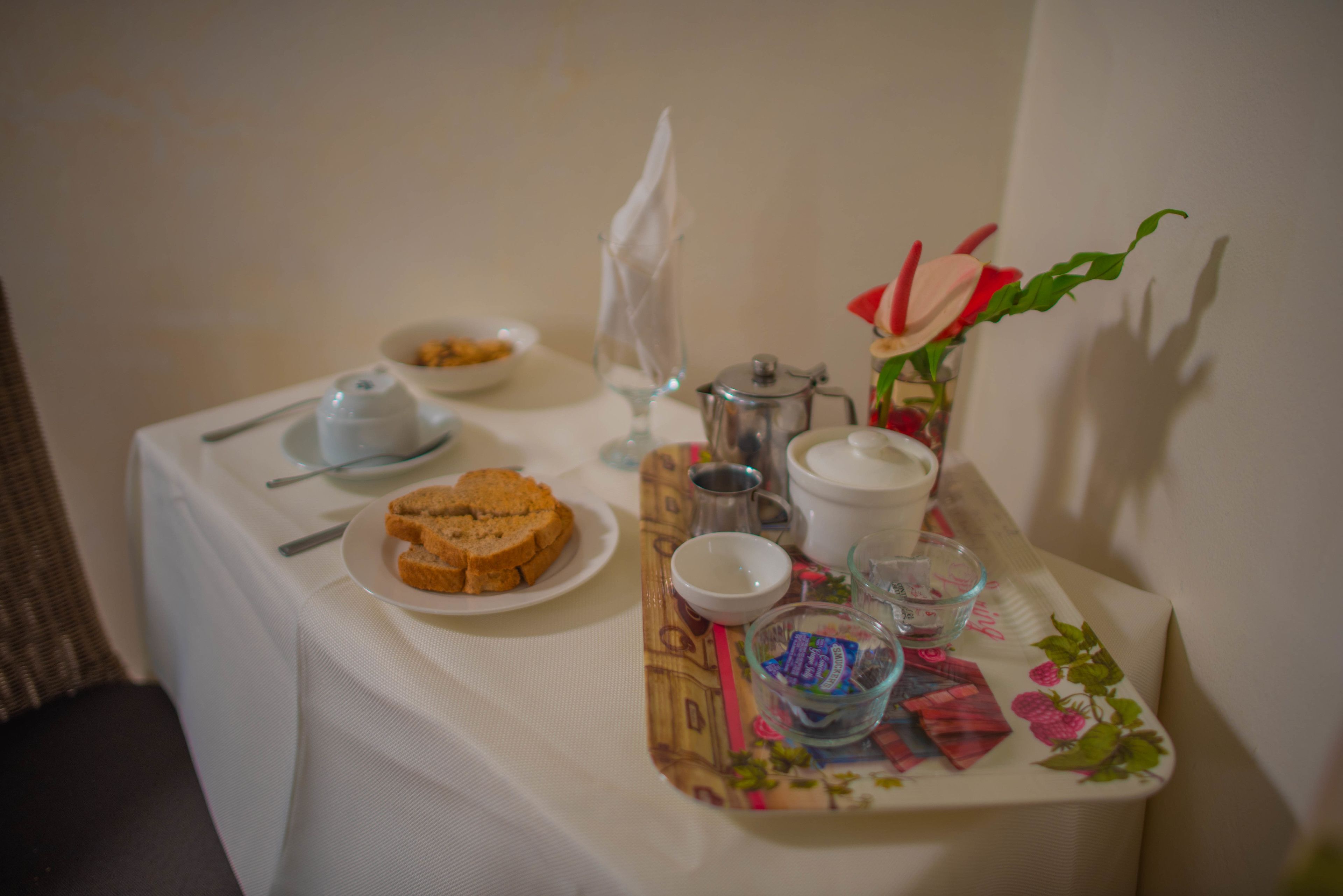 Una mesa de desayuno con pan, una tetera, tazas y un pequeño jarrón con flores.