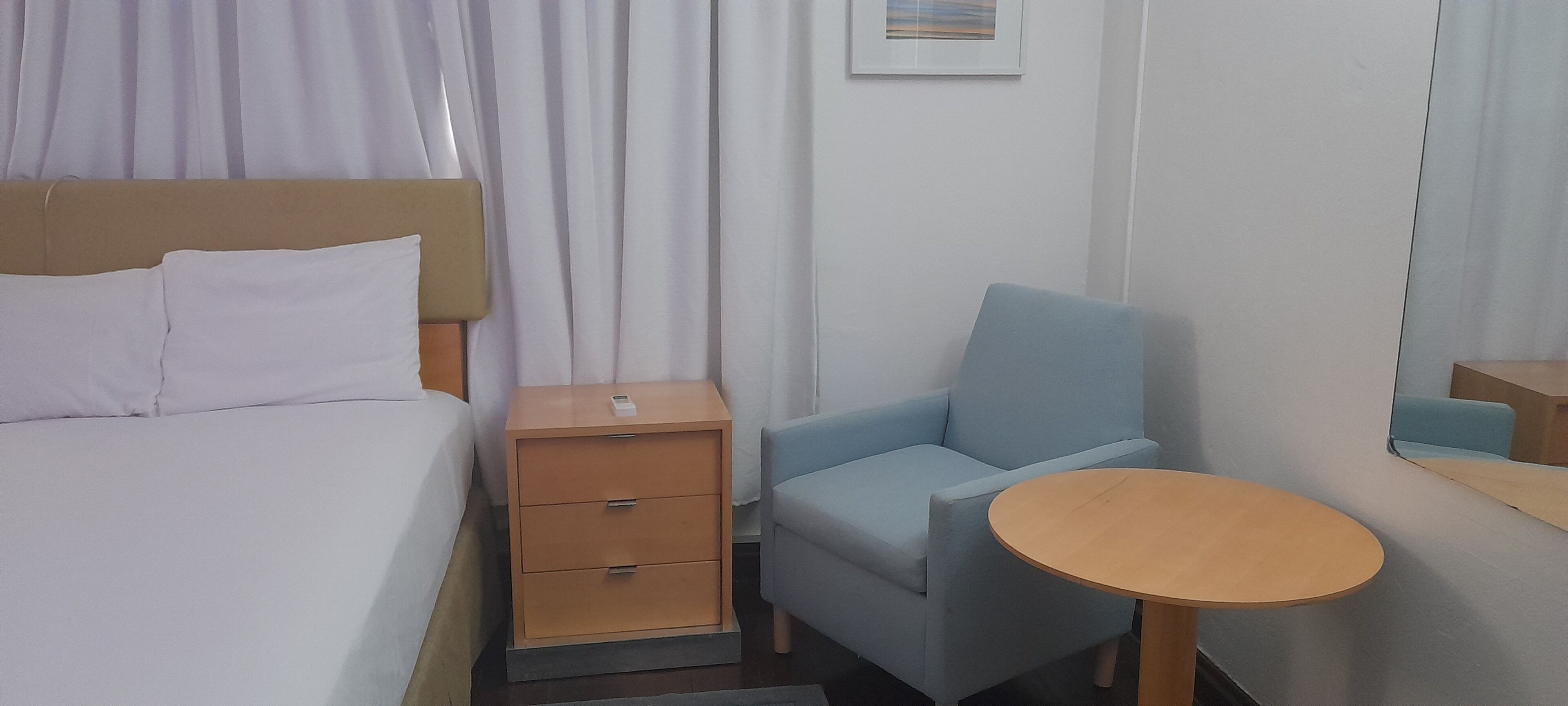 A hotel room with a bed, a nightstand, a chair, and a small table.