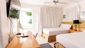 A hotel room with two beds, a desk with a lamp, a ceiling fan, and a window with curtains. - Ocean's Edge Lodge Restaurant & Bar C (Roseau)