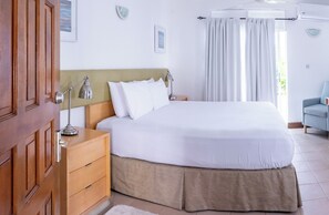 A neatly arranged bedroom with a bed, bedside table, lamp, and a chair. - Ocean's Edge Lodge Restaurant & Bar C (Roseau)