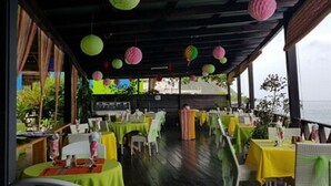 An outdoor dining area with tables covered in yellow tablecloths, surrounded by wicker chairs, and decorated with hanging paper lanterns. - Ocean's Edge Lodge Restaurant & Bar C (Roseau)