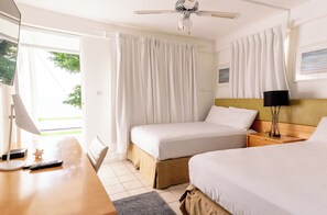 A hotel room with two beds, a desk with a lamp, a ceiling fan, and a window with curtains. - Ocean's Edge Lodge Restaurant & Bar C (Roseau)