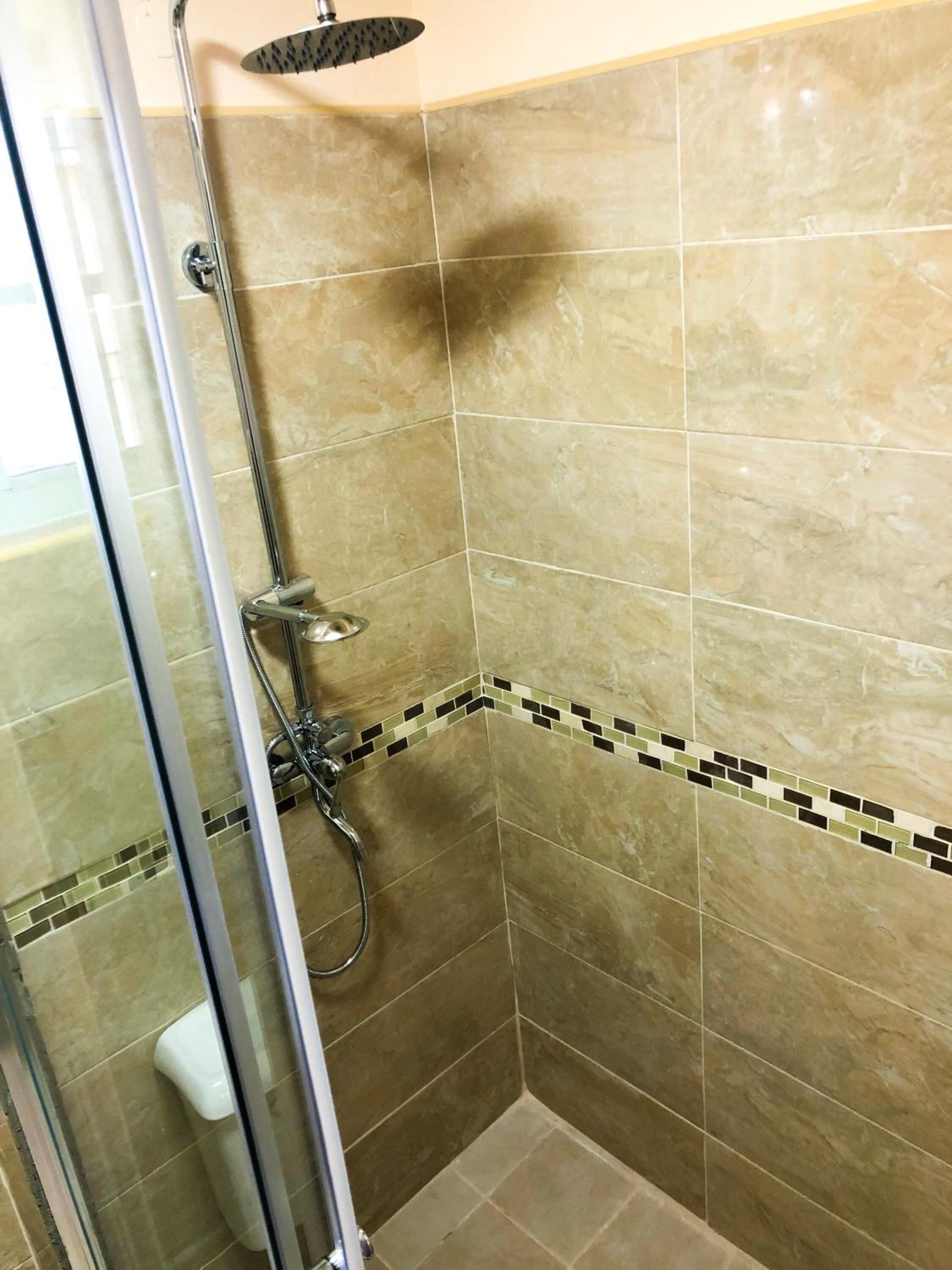 Une douche avec une porte en verre, un pommeau de douche à main et un robinet mural.