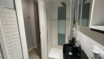 A modern bathroom with a glass shower enclosure, a black sink, and a white tiled floor.