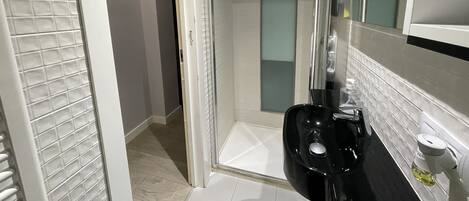 A modern bathroom with a glass shower enclosure, a black sink, and a white tiled floor.