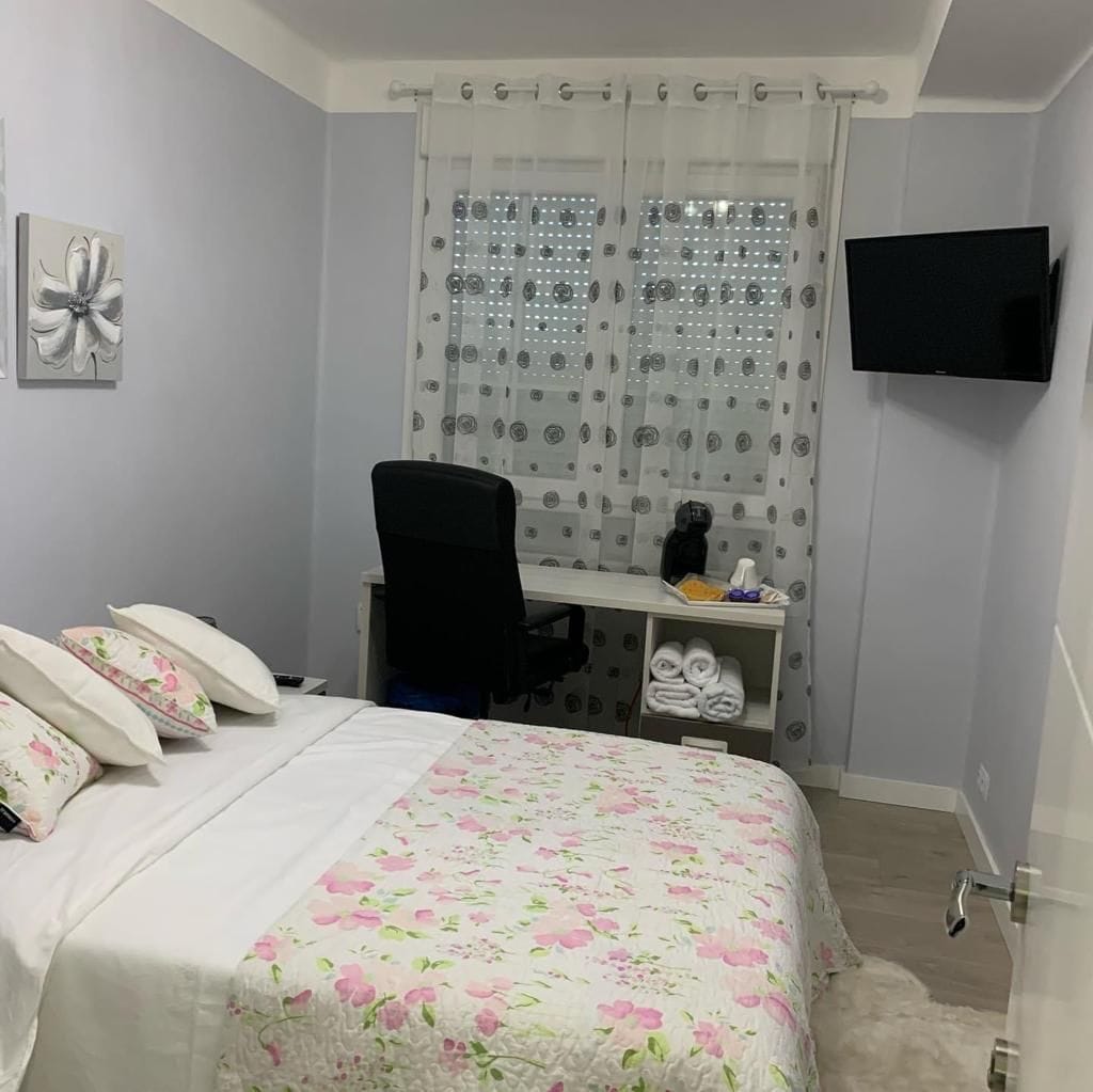 A bedroom with a bed, a desk, a chair, a television, and a shower curtain.