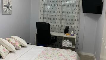 A bedroom with a bed, a desk, a chair, a television, and a shower curtain.