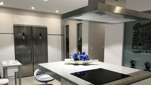 Uma cozinha moderna com ilha central, eletrodomésticos de aço inoxidável e um arranjo decorativo de flores azuis.