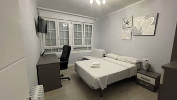 Un dormitorio con cama, escritorio, silla, televisor y obras de arte en la pared.