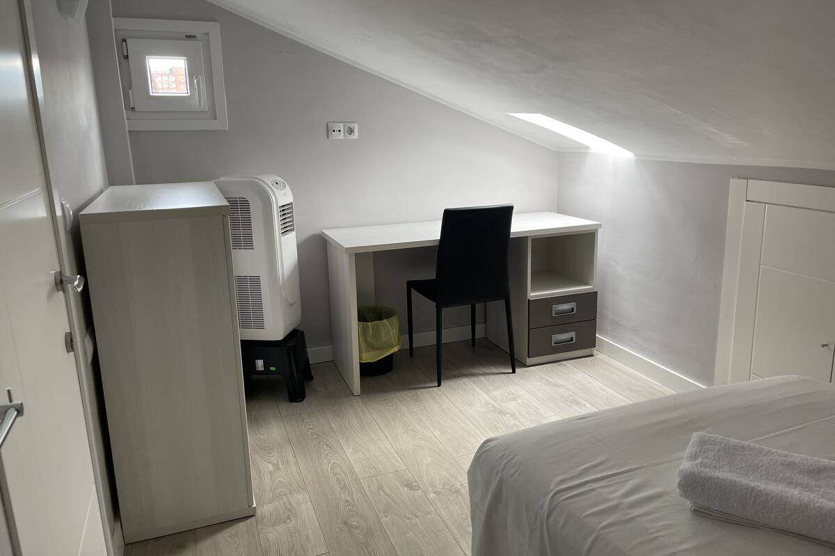 A bedroom with a bed, a desk, a chair, a radiator, and a small window.