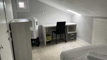 Un dormitorio con cama, escritorio, silla, radiador y una ventana pequeña.