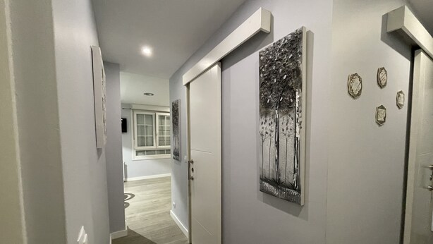 Un pasillo de diseño moderno, con una puerta que presenta una obra de arte de un árbol metálico, un interruptor de luz y un pequeño adorno en la pared.