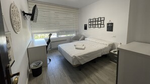 Un dormitorio con cama, escritorio, silla, radiador y ventana con persianas.