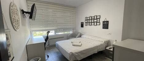 A bedroom with a bed, a desk, a chair, a radiator, and a window with blinds.