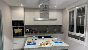 Cozinha moderna com armários brancos, coifa de aço inoxidável, bancada de granito e área de jantar com mesa e cadeiras.