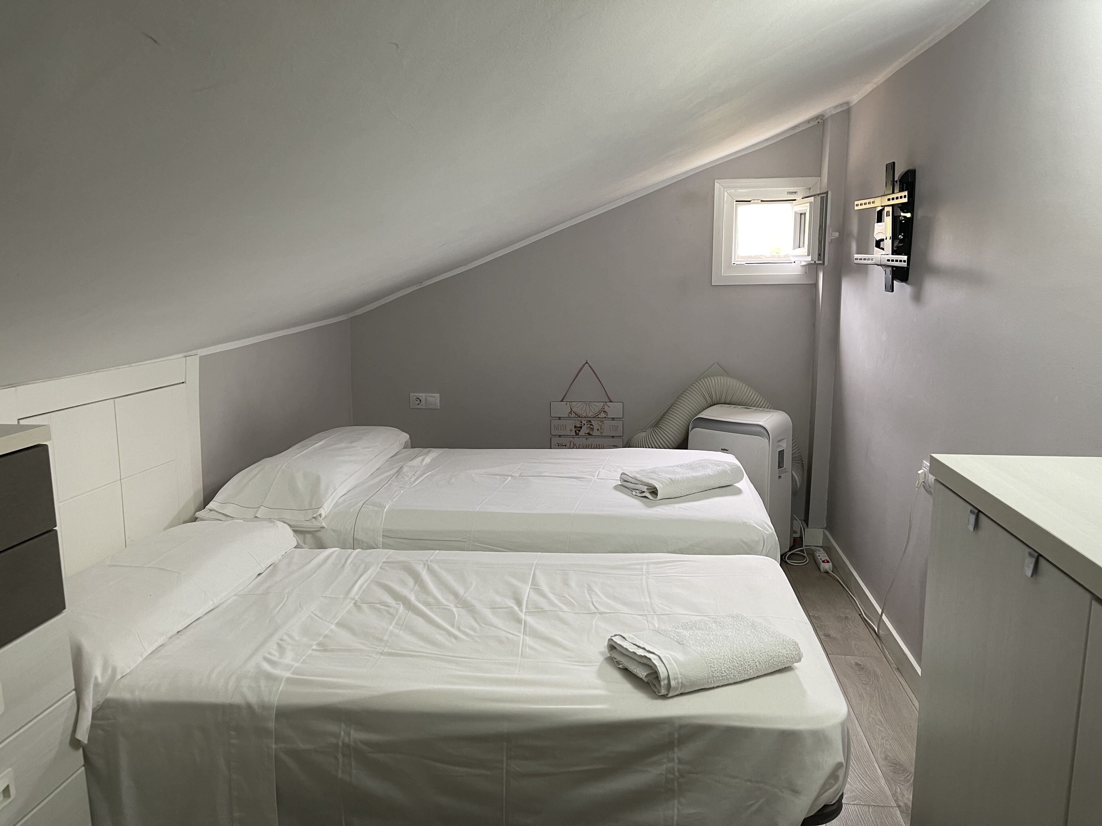 Une petite pièce faiblement éclairée, avec deux lits, un radiateur et une fenêtre.