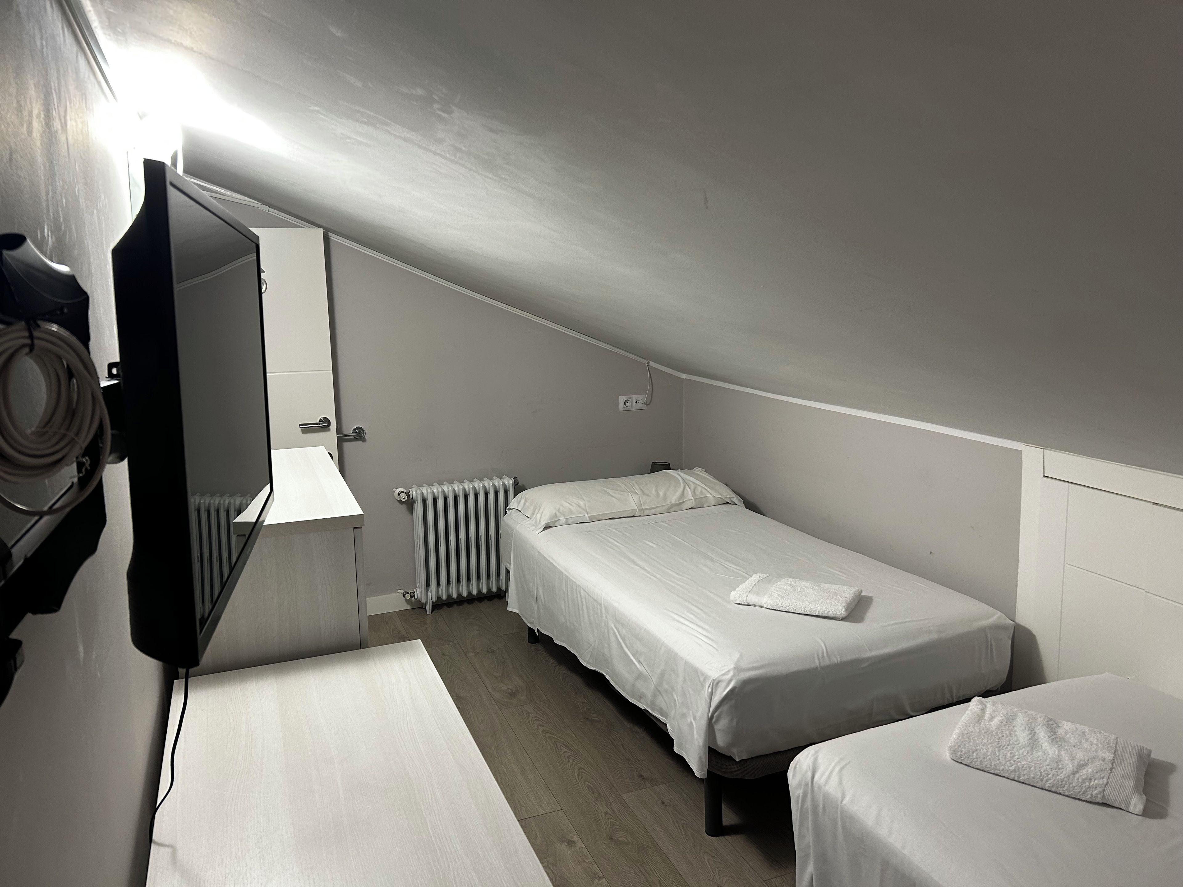 Una habitación pequeña y tenue con dos camas, un radiador y un televisor.