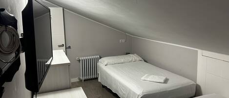 Una habitación pequeña y tenue con dos camas, un radiador y un televisor.
