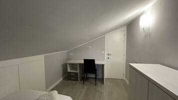 A small, dimly lit attic bedroom with a single bed, a desk, and a chair.