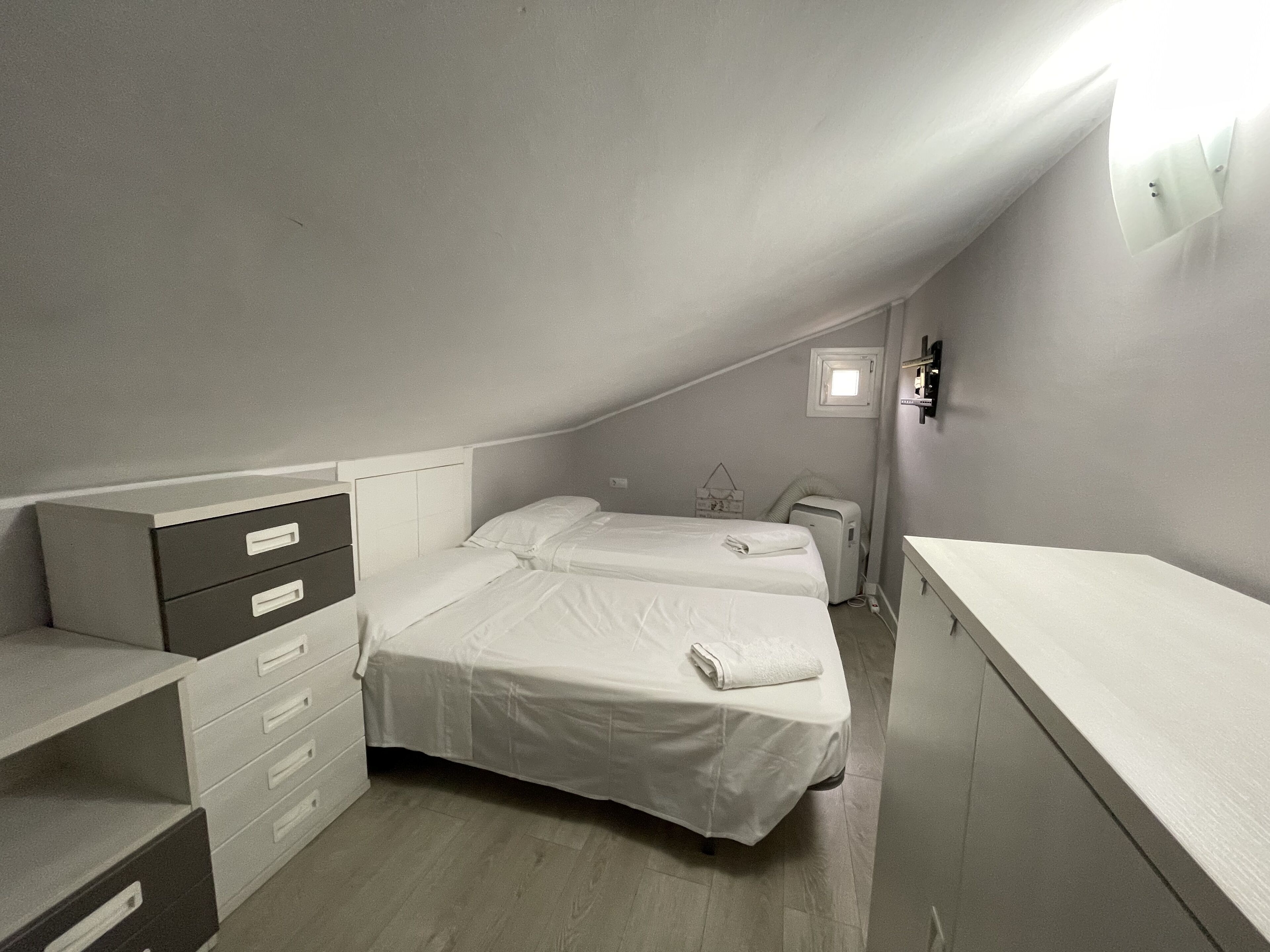 Een kleine, zwak verlichte kamer met twee bedden, een kaptafel en een klein raam.