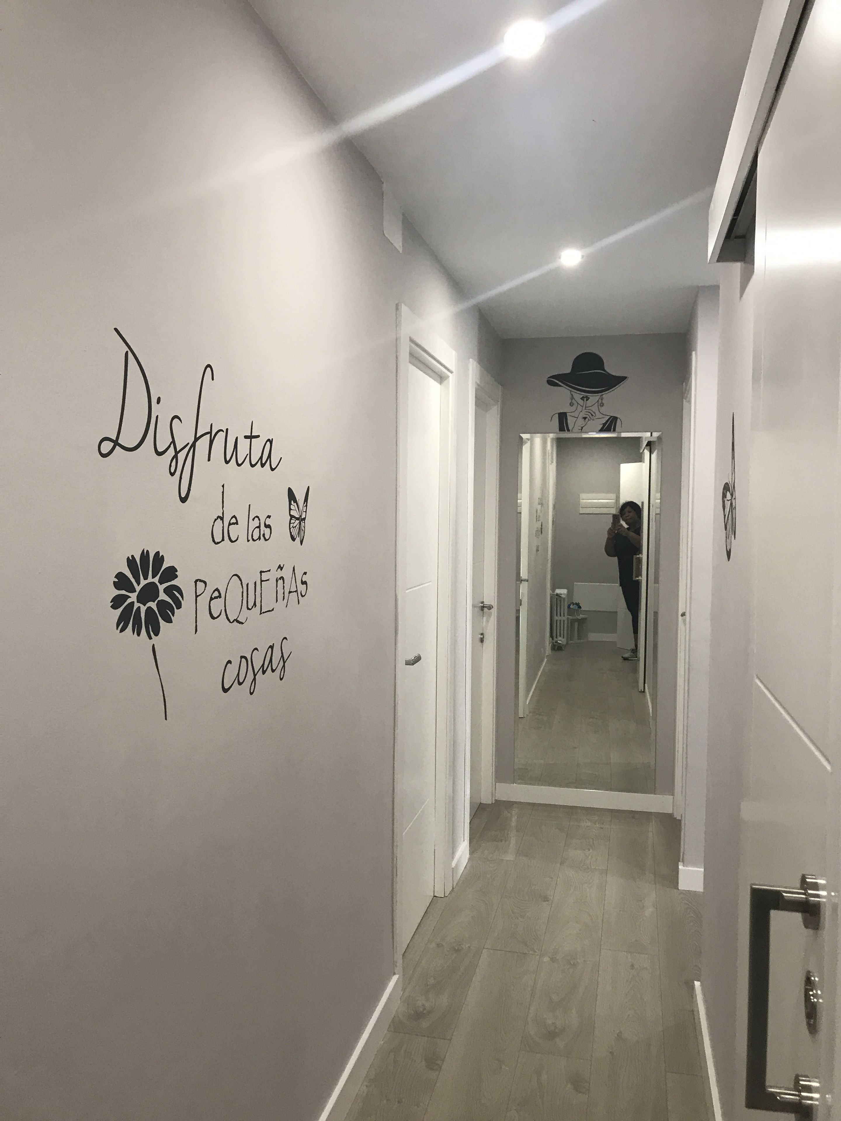 Un pasillo con un muro espejado, un letrero decorativo y una persona tomando una fotografía.