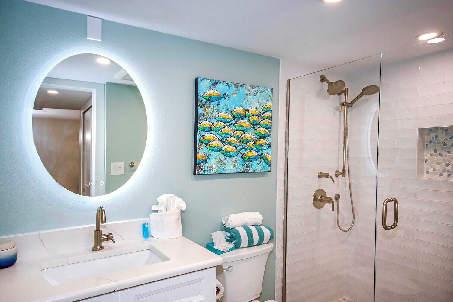 A bathroom with a round mirror, a sink, a toilet, and a shower.