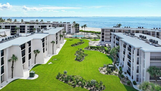 Un hotel moderno con varios pisos, un patio central con césped y plantas, y vistas al océano.