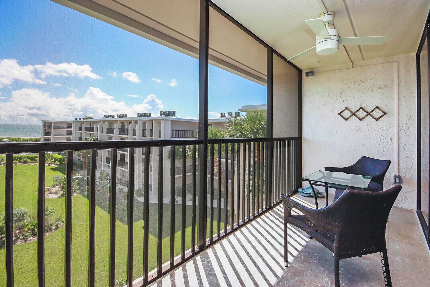 A balcony with a view of a residential area, a table, and two chairs.