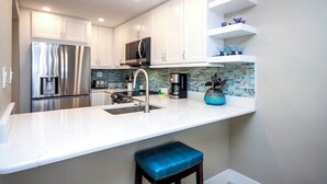 Una cocina moderna con armarios blancos, electrodomésticos de acero inoxidable, un taburete azul y un salpicadero de azulejos.