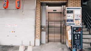 An elevator in a building with a closed shutter door, a brick wall, and a signboard with advertisements. - mizuka Nakasu 1 - unmanned hotel - (Fukuoka)