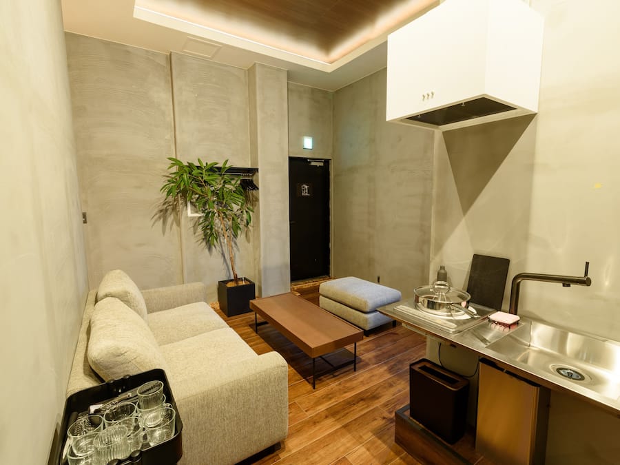 A modern living room with a sofa, a coffee table, a small dining table, and a kitchen area with a sink and stove.