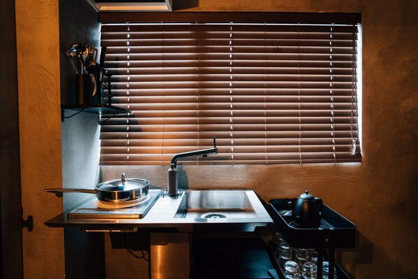 A compact kitchen with a built-in stove, sink, and a window with blinds. - mizuka Nakasu 1 - unmanned hotel - (Fukuoka)