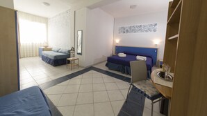 A hotel room with a bed, a desk with a chair, a small table, and a window with curtains.