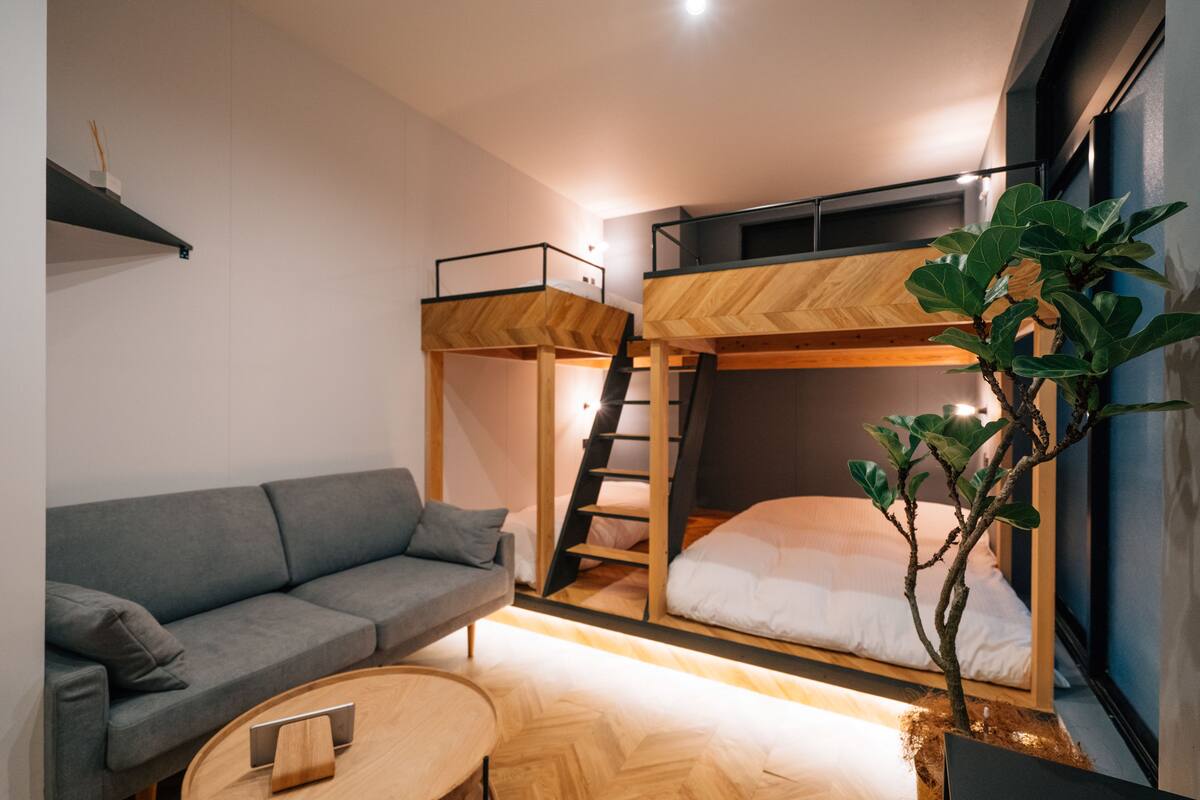 Une petite pièce comprenant un lit superposé, un canapé, une petite table et une plante en pot.