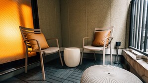 Een moderne, knusse zithoek met twee stoelen en een rond poefje, een klein bijzettafeltje en een raam met uitzicht.