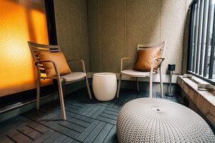 Un rincón moderno y acogedor con dos sillones, un reposapiés redondo, una mesita auxiliar y una ventana con vistas.