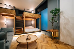 Una habitación moderna con cama de altillo, sofá, mesa redonda de madera y una planta en maceta.
