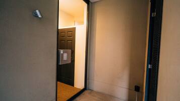 A narrow hallway with a door leading to a room. The hallway has a light switch and a door handle on the wall.