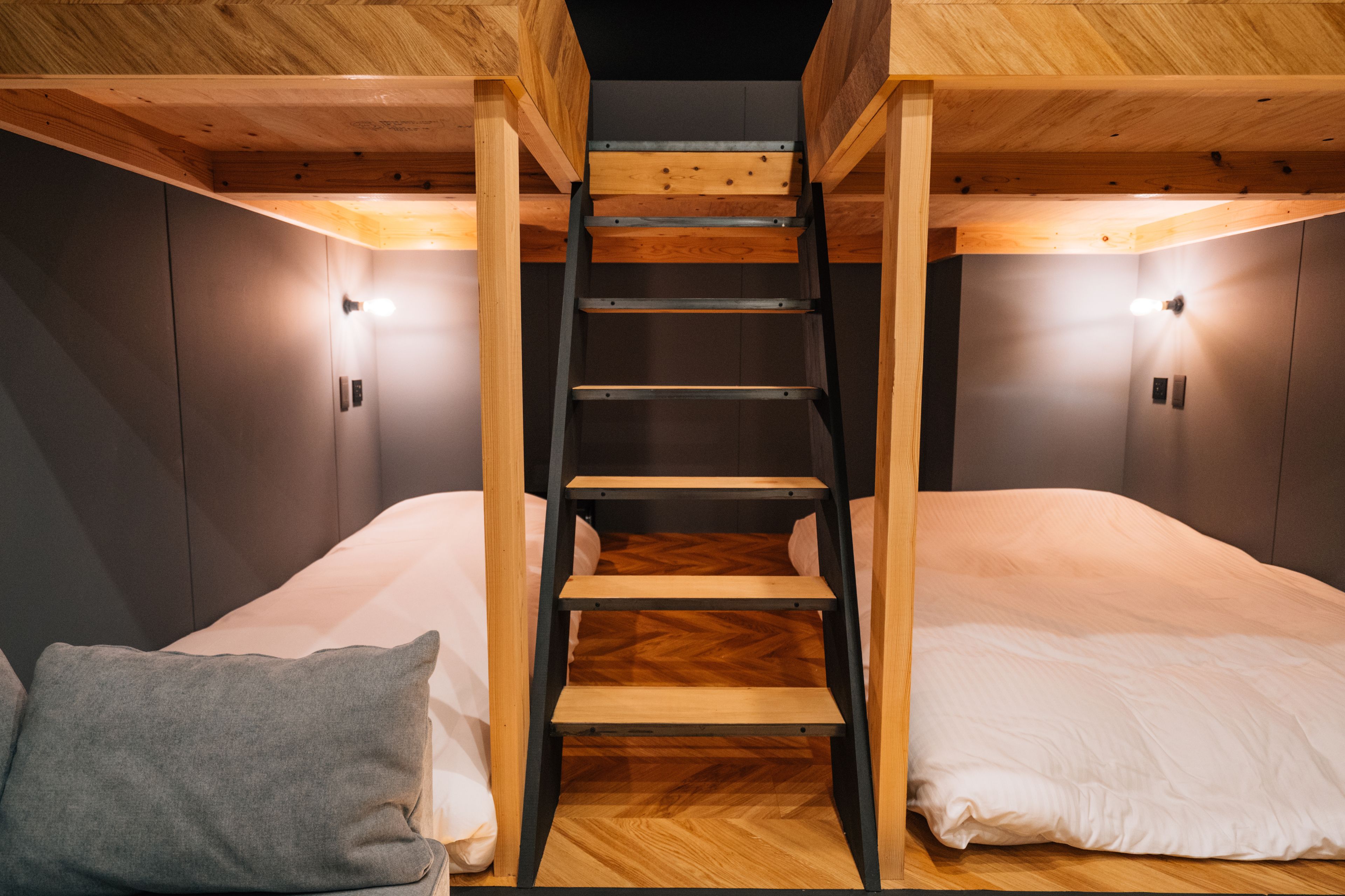 A bunk bed with a wooden ladder, two bedside lamps, and a grey pillow.