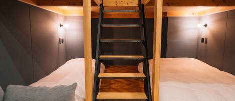 A bunk bed with a wooden ladder, two bedside lamps, and a grey pillow.