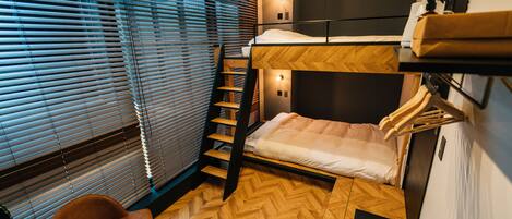 Una habitación pequeña con una cama litera, suelo de madera, una silla y una mesita.