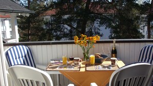 Una terraza con una mesa lista para el desayuno, incluyendo sillas, una botella de champán y un jarrón de flores.
