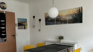 Comedor con una mesa negra y sillas amarillas, una lámpara colgante blanca y un cuadro de una puesta de sol.