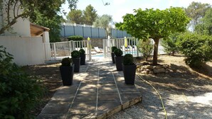 Caminho que leva a uma área de piscina, com plantas em vasos e um cercado branco.