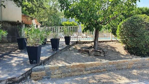 Uma área externa ajardinada com vasos de plantas, um muro de pedra de contenção e uma área de piscina com espreguiçadeiras.