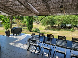 En udendørs terrasse med et overdækket siddeområde, grill og plantekasser.