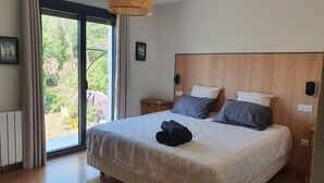 Quarto com cama grande, cabeceira de madeira e vista para o verde lá fora.
