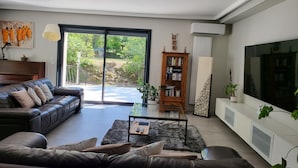 Uma sala de estar moderna com um sofá de couro, uma mesa de centro, uma estante de livros e uma televisão grande.